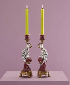 two candles are sitting next to each other on a purple surface with a pink background