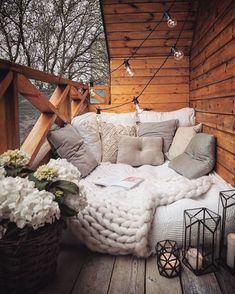 an outdoor bed with blankets and pillows on the outside deck, surrounded by candles and flowers