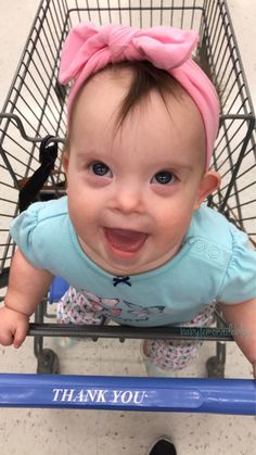 a baby sitting in a shopping cart with a pink bow on her head