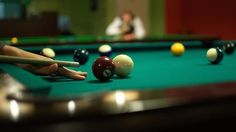 a pool table with several billards and two people in the background