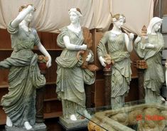 four statues of women are on display in a glass case