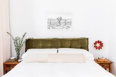 a bed with white linens and green headboard next to a painting on the wall