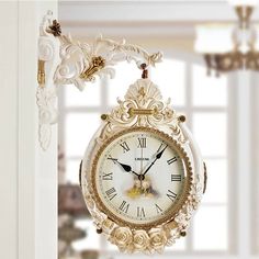 an ornate clock hanging from the side of a wall in front of a window with white curtains