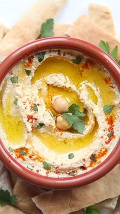 hummus in a red bowl with pita bread and garnish on the side