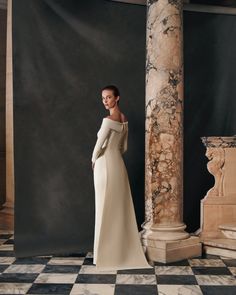 a woman in a white dress standing next to an ornate column and marble flooring