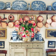 an old dresser with plates and vases on it in front of a wall full of pictures