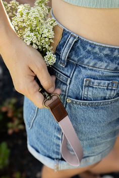 a woman is holding flowers in her jeans pocket while wearing a belt with an attached strap