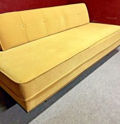 a yellow couch sitting on top of a floor next to a red wall in a room