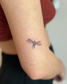 a woman's arm with a small tattoo of a dragonfly on the left side