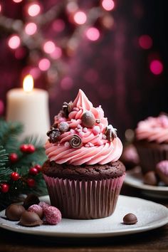 cupcakes with pink frosting and chocolate candies on plates next to a lit candle