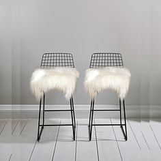 two black barstools with white fur on them in front of a gray wall