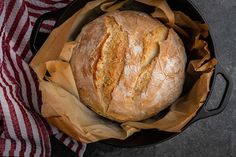 a loaf of bread in a black pan on a red and white striped towel next to a wooden spoon