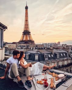 a man and woman sitting on top of a roof next to the eiffel tower