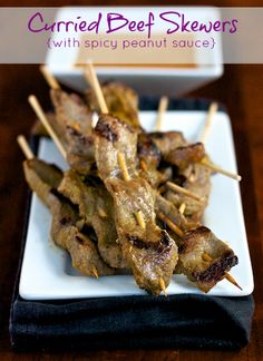 several skewers of food on a white plate with dipping sauce in the background