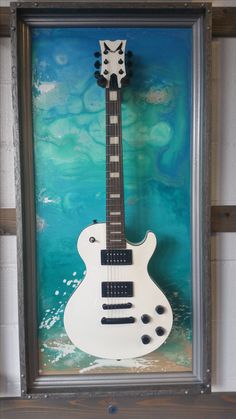 a white electric guitar is mounted in a shadow box on the wall next to a blue and green background