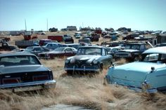 many old cars are parked in a field with grass and dirt on the ground,