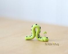 a green toy snake sitting on top of a wooden table next to a small flower