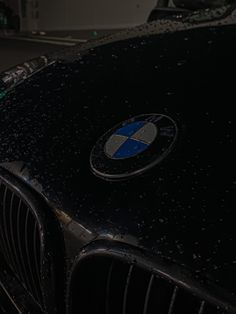 the front end of a black bmw car with rain drops on it's hood