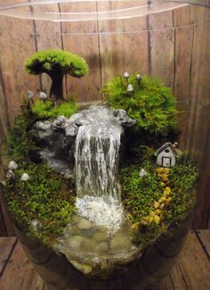 an aquarium with moss, rocks and water flowing from the top to the bottom in front of a wooden wall