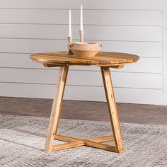 a wooden table with two white candles on it and a rug in front of it