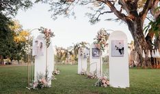 an outdoor ceremony setup with flowers and pictures on the back of white pillars in front of a tree