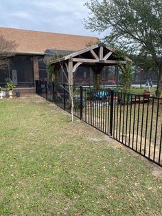 a black fence in front of a house with a tree and grass area next to it