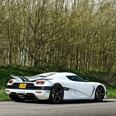 the white sports car is parked on the side of the road in front of some trees