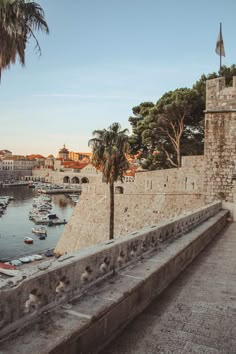 an old stone wall next to a body of water with boats in it and palm trees on the other side