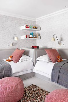 two beds in a room with pink and gray pillows on them, one has a teddy bear