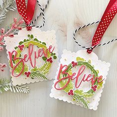 two christmas ornament hanging on a wooden table with red ribbon and holly decorations