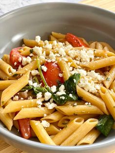 a pasta dish with tomatoes, spinach and feta cheese in a gray bowl