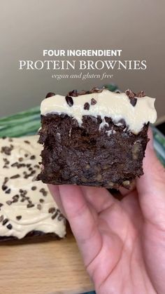 a hand holding a piece of brownie with white frosting