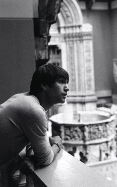 black and white photograph of a young man leaning on a railing looking out at the city