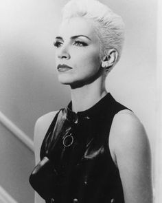 a black and white photo of a woman with short hair wearing a leather dress, looking off to the side