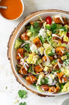 a white bowl filled with lettuce, tomatoes and dressing on top of a table