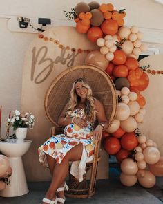 a woman is sitting in a chair with balloons on the wall behind her and an orange balloon arch