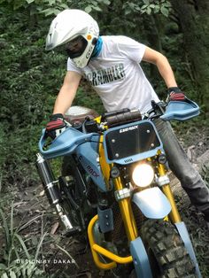 a man riding on the back of a blue motorcycle down a dirt road next to trees