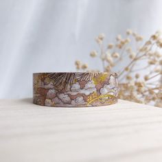 a close up of a bracelet on a table with flowers and plants in the background