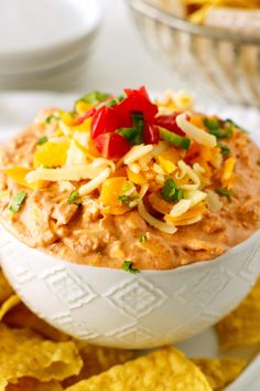 a white bowl filled with cheese salsa dip surrounded by tortilla chips on the side