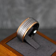 a wedding band with two tone gold and silver inlays is displayed on a wooden stand