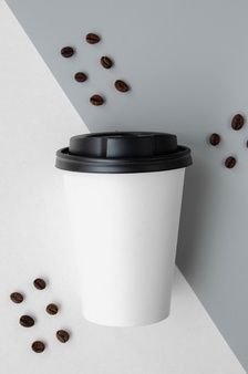 a coffee cup sitting on top of a white table next to some coffee beans that are scattered around it