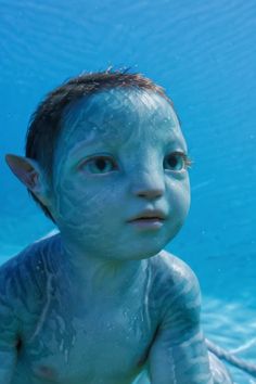 a young boy with blue paint on his face and body in the water, looking at the camera