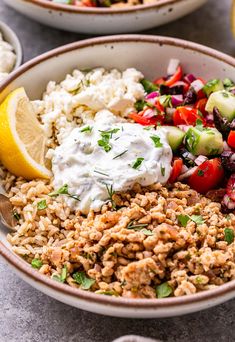 a bowl filled with rice, cucumbers, tomatoes and other vegetables next to lemon wedges