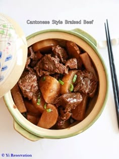 a bowl filled with beef and potatoes next to chopsticks on a white surface