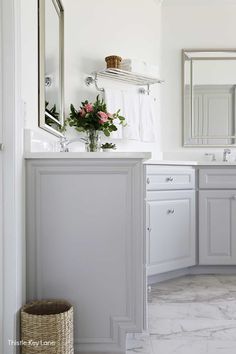 a bathroom with marble floors and white cabinets, flowers on the sink counter top and mirror above it