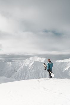 a man standing on top of a snow covered slope holding a snowboard in his hand