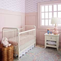 a baby's room with pink walls and white crib next to a window