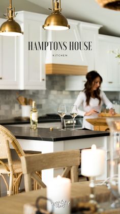 a woman standing in a kitchen next to a table with wine glasses on top of it