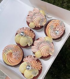 four cupcakes in a white box with pink and yellow frosting