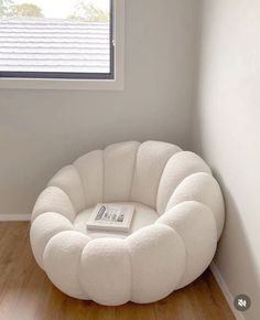 a white chair sitting in front of a window next to a book on top of a wooden floor